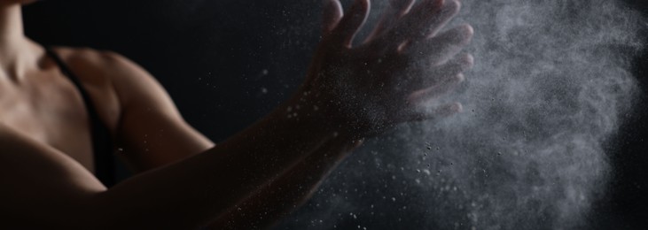 Photo of Woman clapping hands with talcum powder before training on black background, closeup