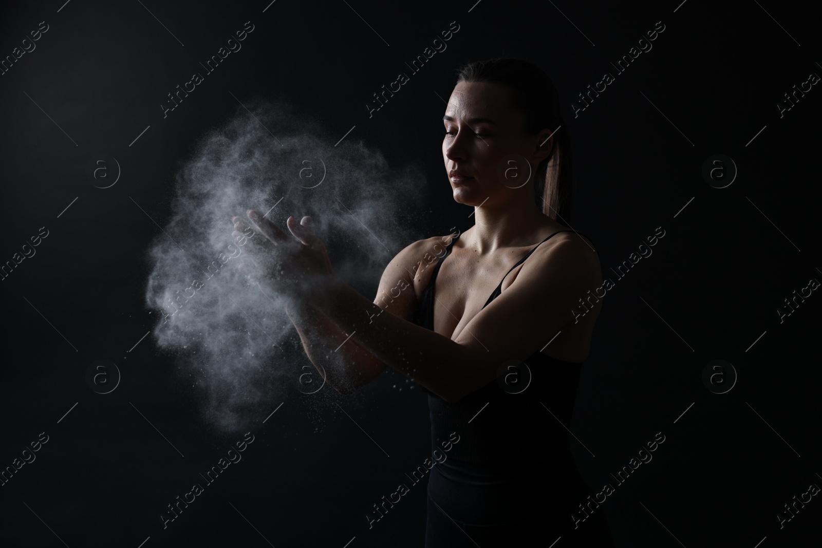 Photo of Woman clapping hands with talcum powder before training on black background