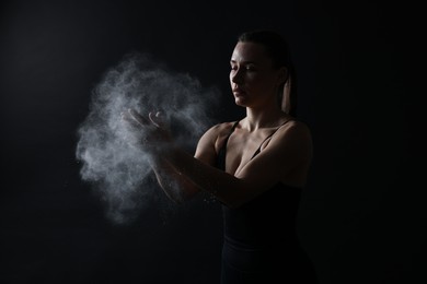 Photo of Woman clapping hands with talcum powder before training on black background