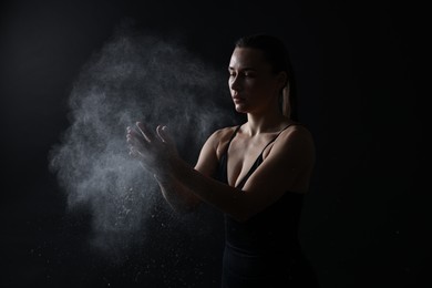 Photo of Woman clapping hands with talcum powder before training on black background