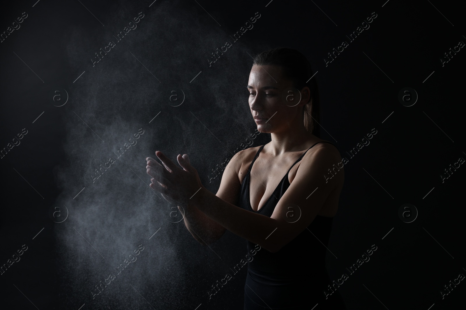 Photo of Woman clapping hands with talcum powder before training on black background