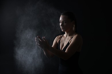 Photo of Woman clapping hands with talcum powder before training on black background