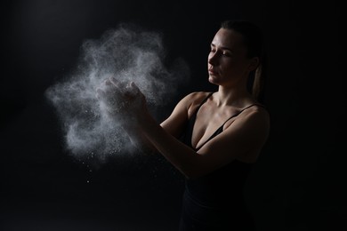 Photo of Woman clapping hands with talcum powder before training on black background