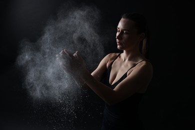 Photo of Woman clapping hands with talcum powder before training on black background