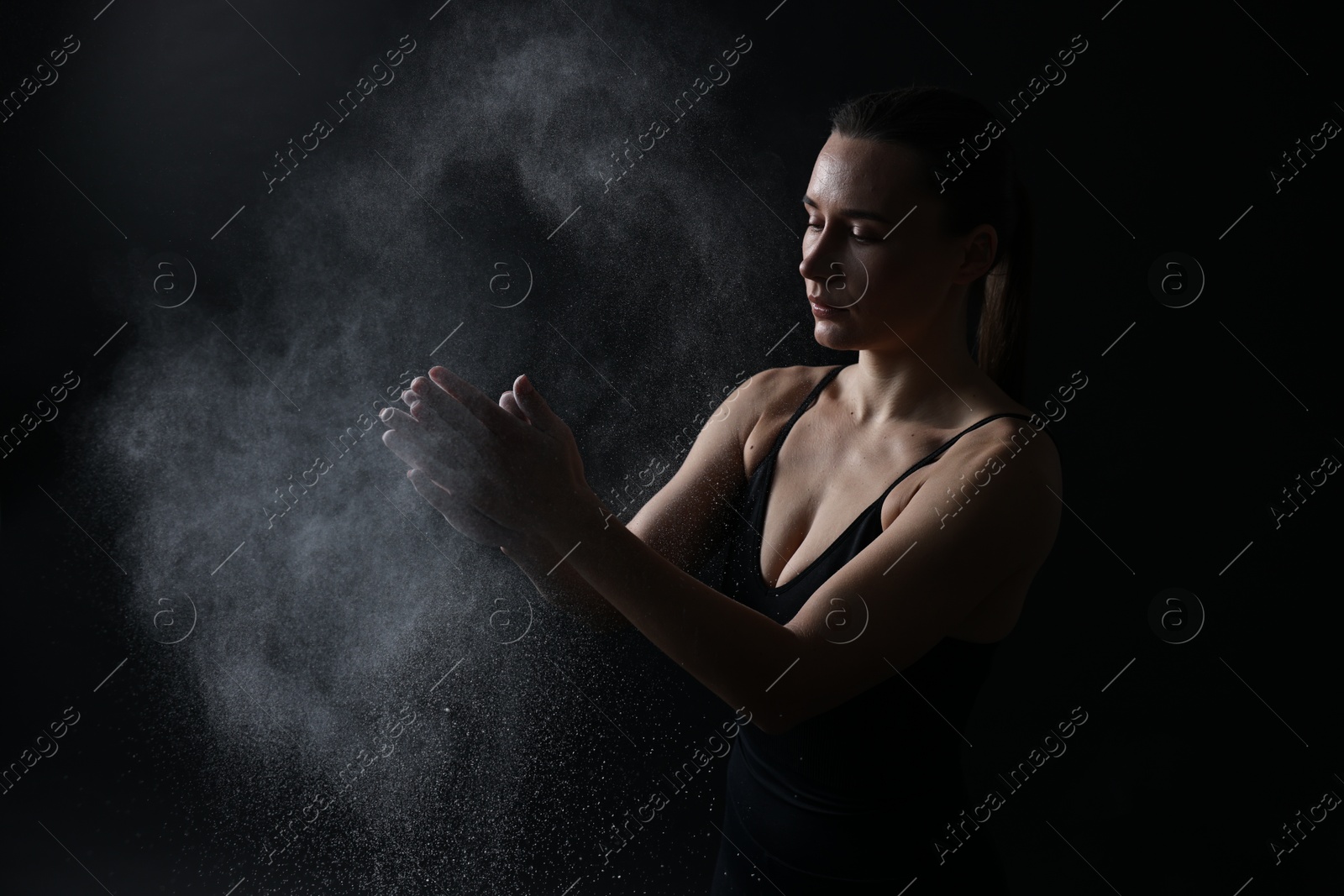 Photo of Woman clapping hands with talcum powder before training on black background