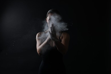 Photo of Woman clapping hands with talcum powder before training on black background