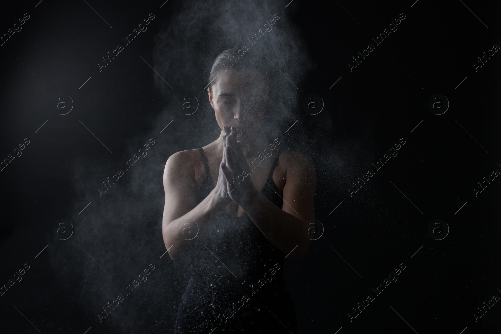 Photo of Woman clapping hands with talcum powder before training on black background