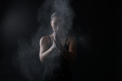 Photo of Woman clapping hands with talcum powder before training on black background