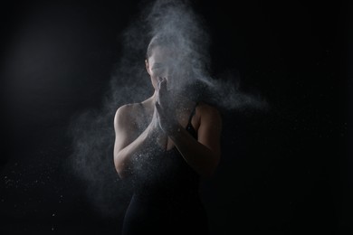 Photo of Woman clapping hands with talcum powder before training on black background