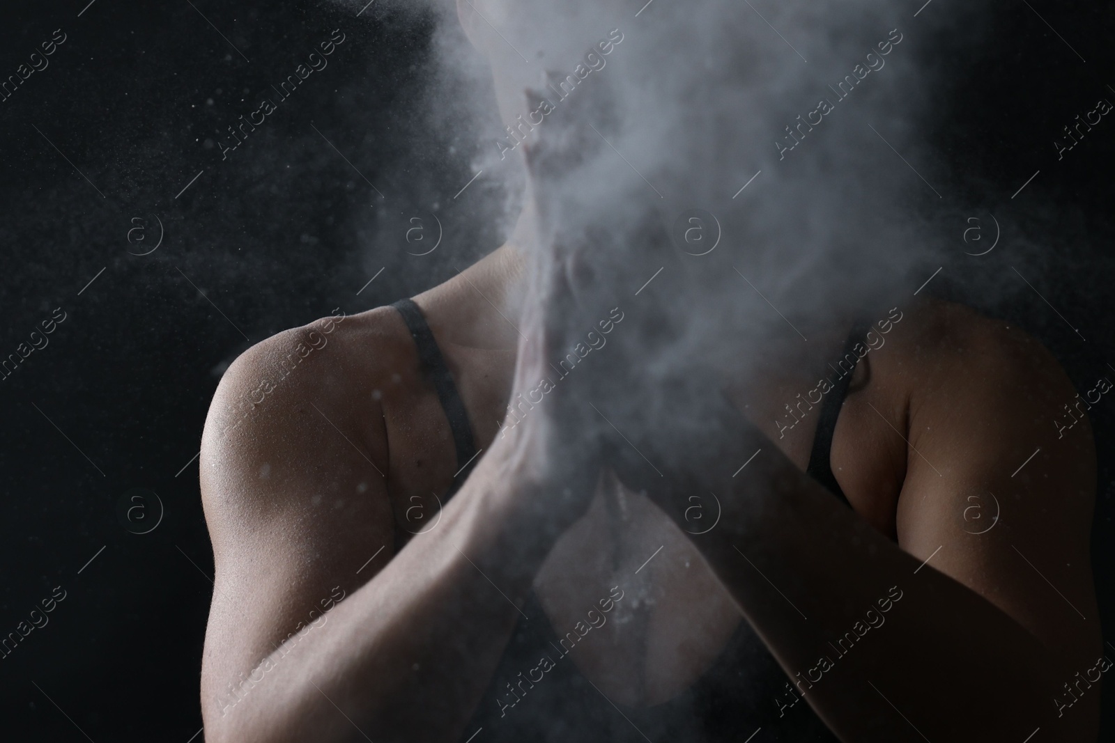 Photo of Woman clapping hands with talcum powder before training on black background, closeup