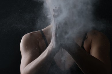 Photo of Woman clapping hands with talcum powder before training on black background, closeup