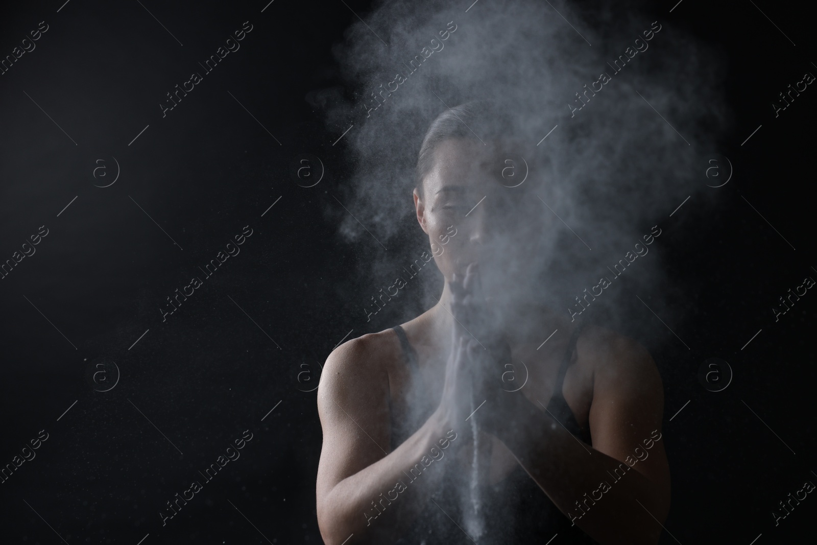 Photo of Woman clapping hands with talcum powder before training on black background, space for text