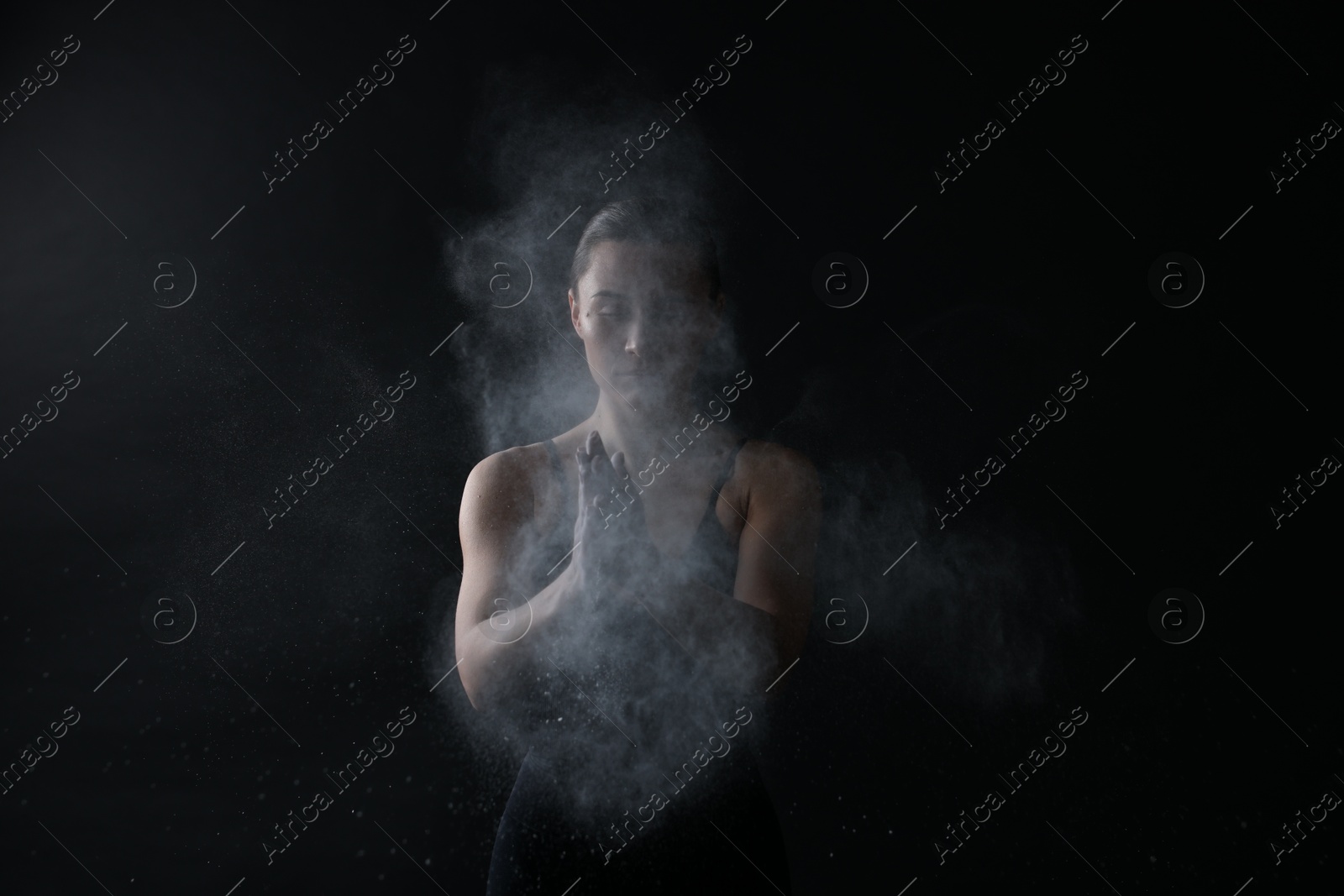 Photo of Woman clapping hands with talcum powder before training on black background