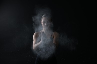 Photo of Woman clapping hands with talcum powder before training on black background