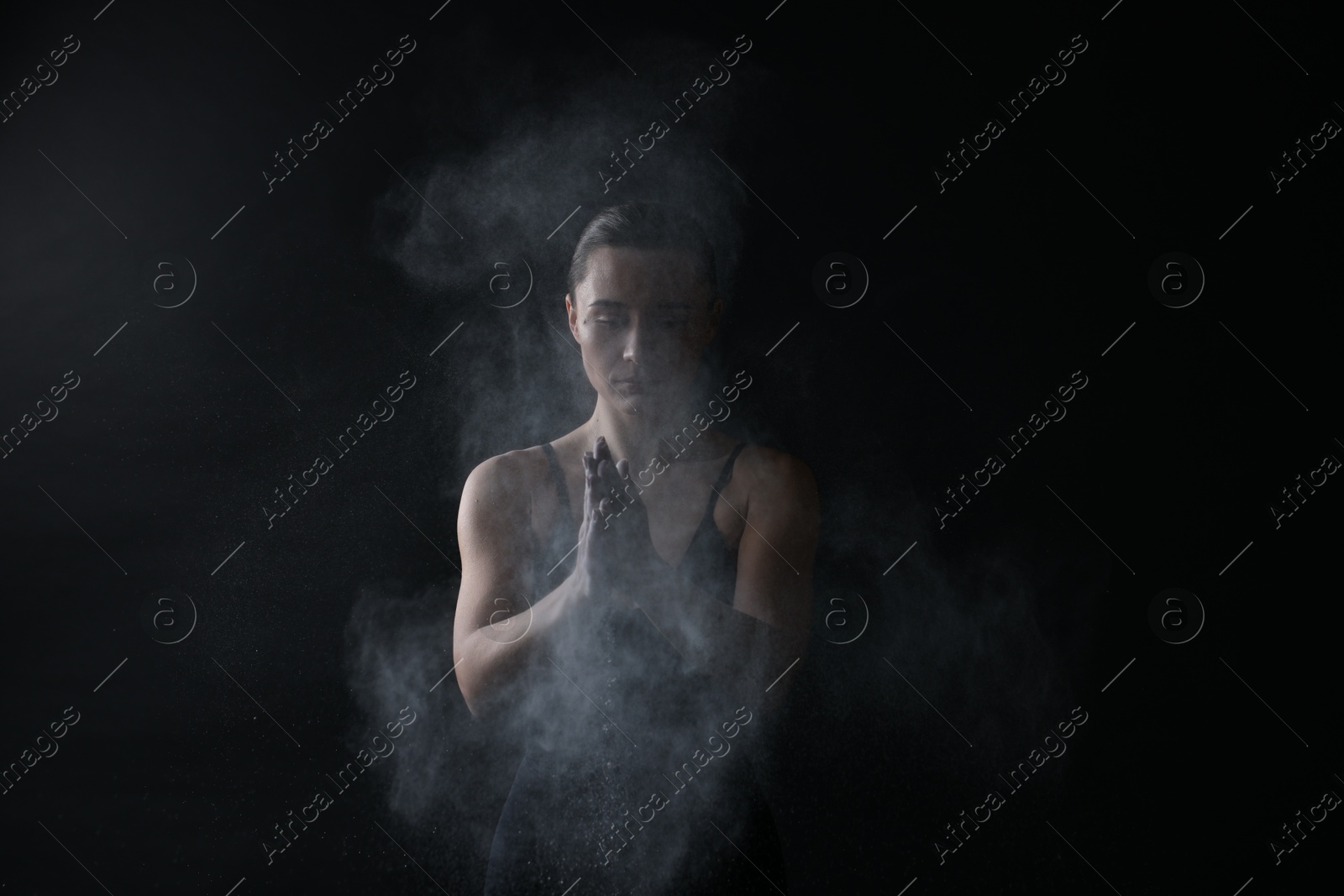 Photo of Woman clapping hands with talcum powder before training on black background