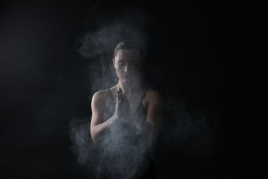 Photo of Woman clapping hands with talcum powder before training on black background