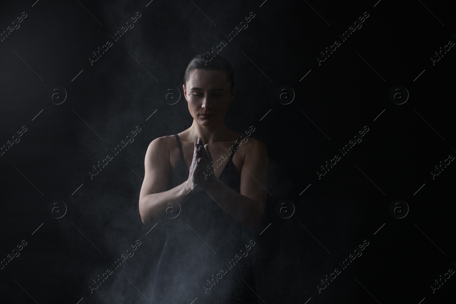 Photo of Woman clapping hands with talcum powder before training on black background