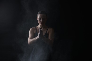 Photo of Woman clapping hands with talcum powder before training on black background