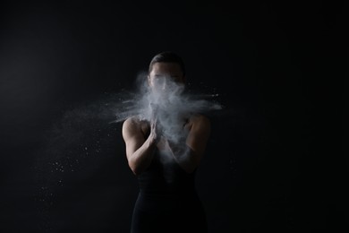 Photo of Woman clapping hands with talcum powder before training on black background