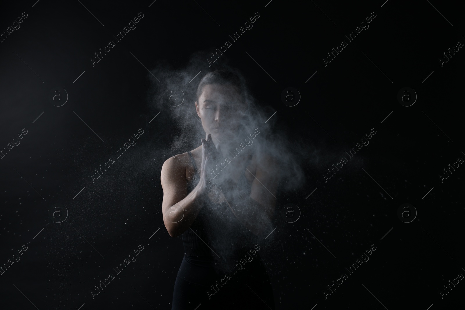 Photo of Woman clapping hands with talcum powder before training on black background