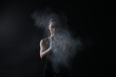 Photo of Woman clapping hands with talcum powder before training on black background