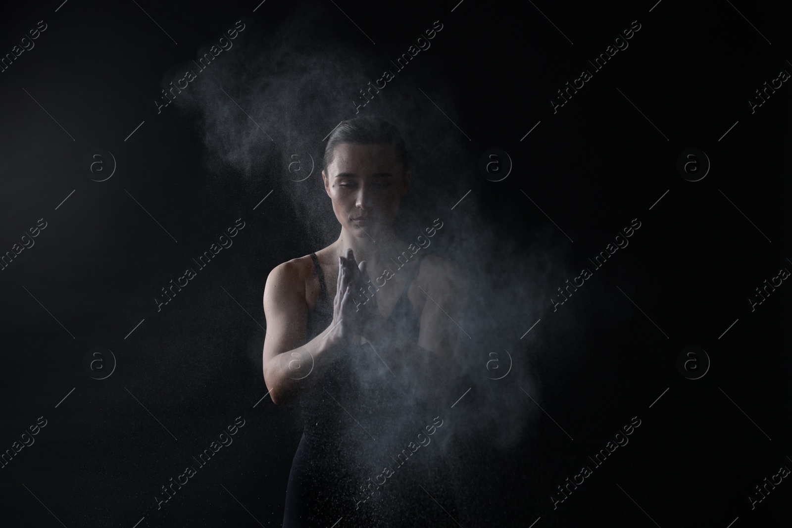 Photo of Woman clapping hands with talcum powder before training on black background