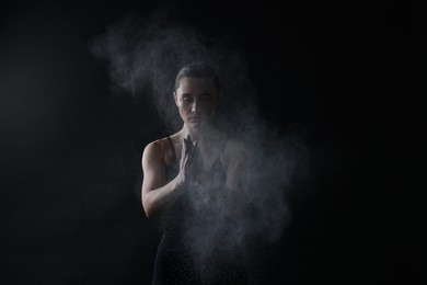 Photo of Woman clapping hands with talcum powder before training on black background