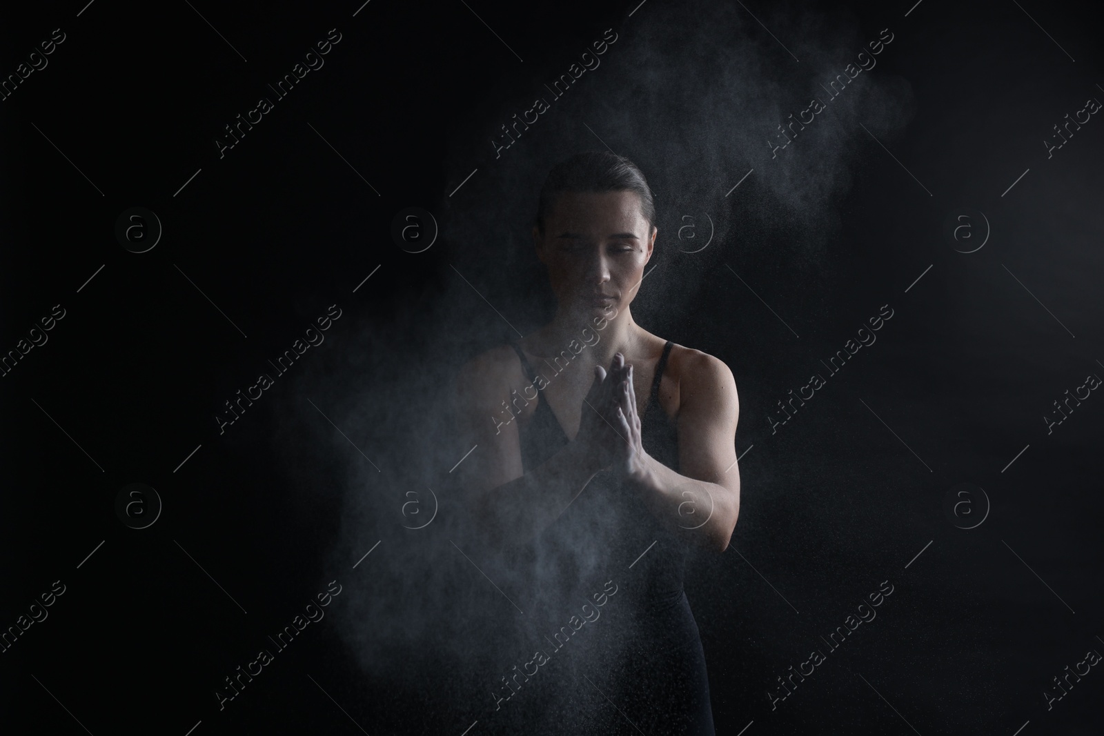 Photo of Woman clapping hands with talcum powder before training on black background