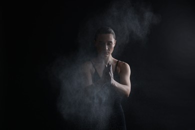 Photo of Woman clapping hands with talcum powder before training on black background