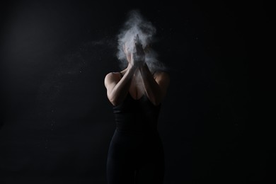 Photo of Woman clapping hands with talcum powder before training on black background