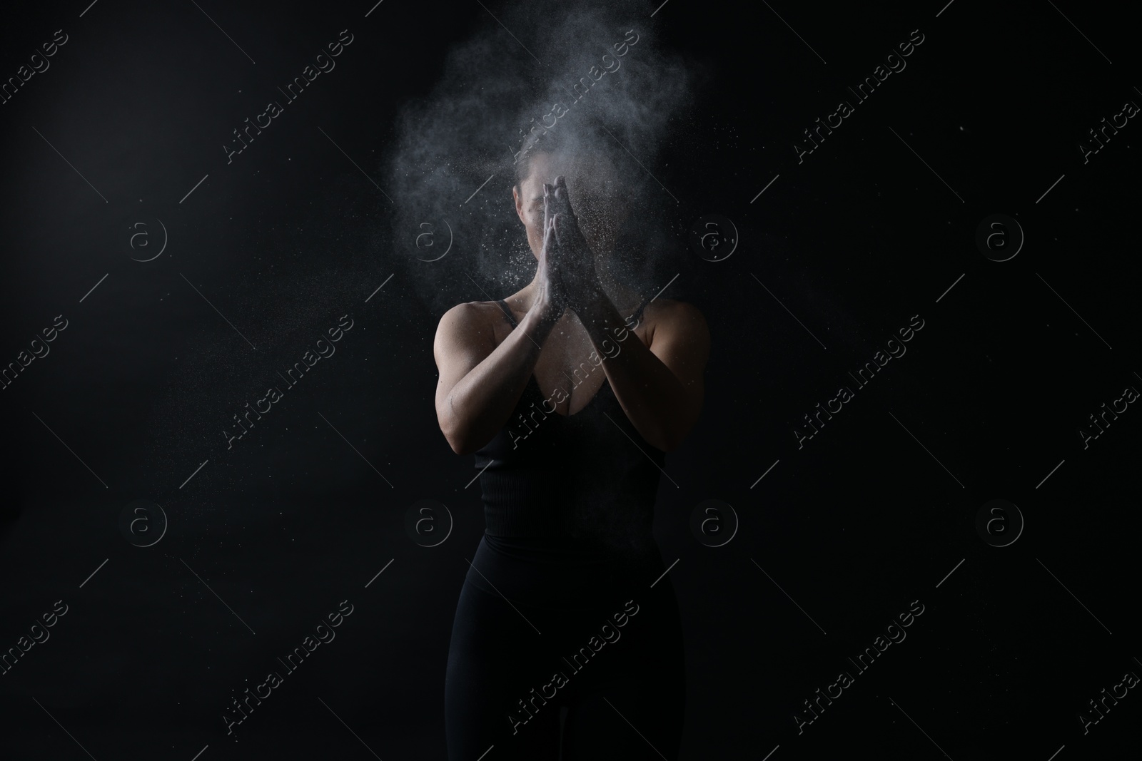 Photo of Woman clapping hands with talcum powder before training on black background