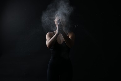 Photo of Woman clapping hands with talcum powder before training on black background