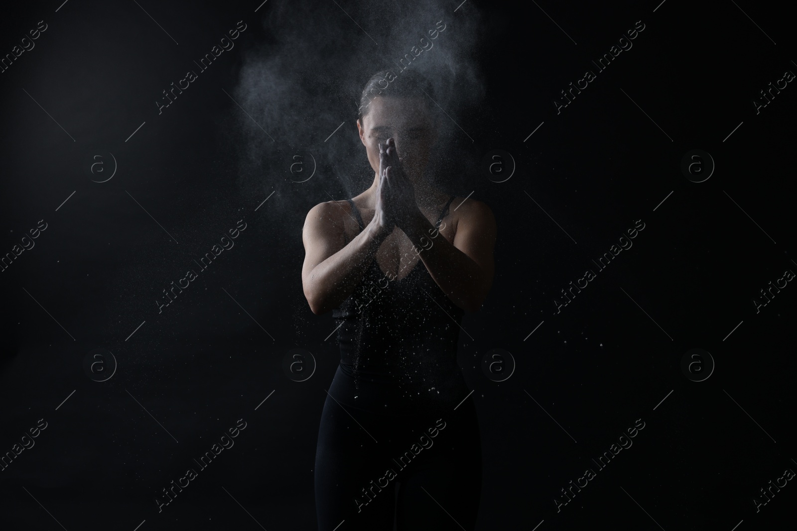 Photo of Woman clapping hands with talcum powder before training on black background