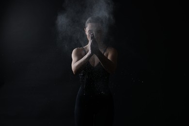 Photo of Woman clapping hands with talcum powder before training on black background