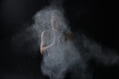 Photo of Woman clapping hands with talcum powder before training on black background