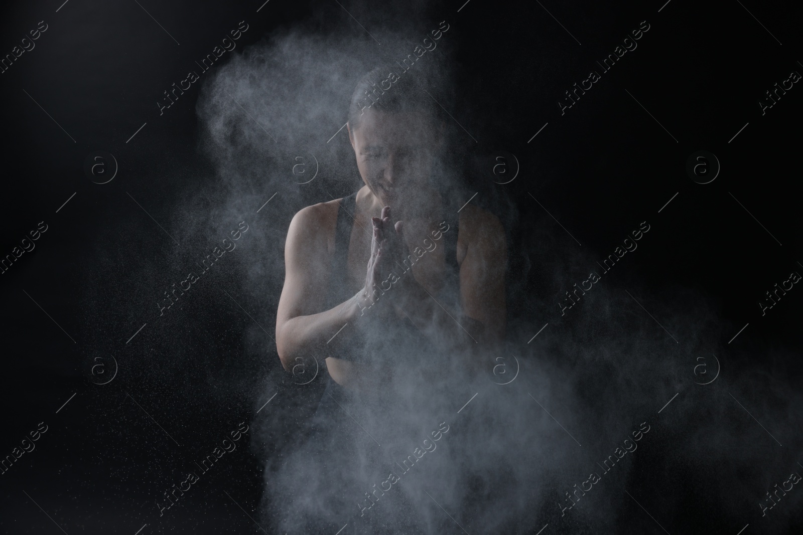 Photo of Woman clapping hands with talcum powder before training on black background