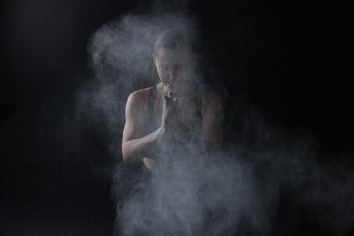 Photo of Woman clapping hands with talcum powder before training on black background