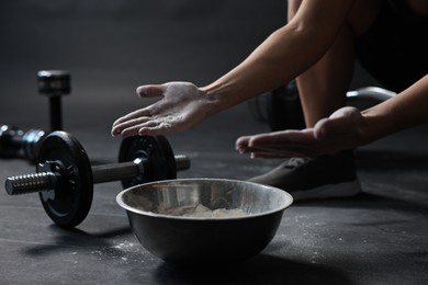 Photo of Woman applying talcum powder onto her hands above bowl before training in gym, closeup