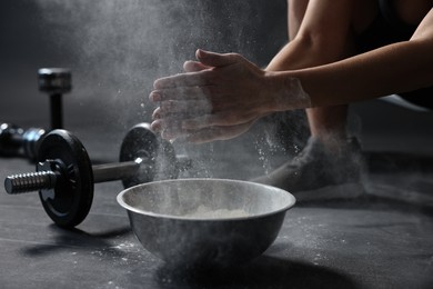 Photo of Woman clapping hands with talcum powder above bowl before training in gym, closeup