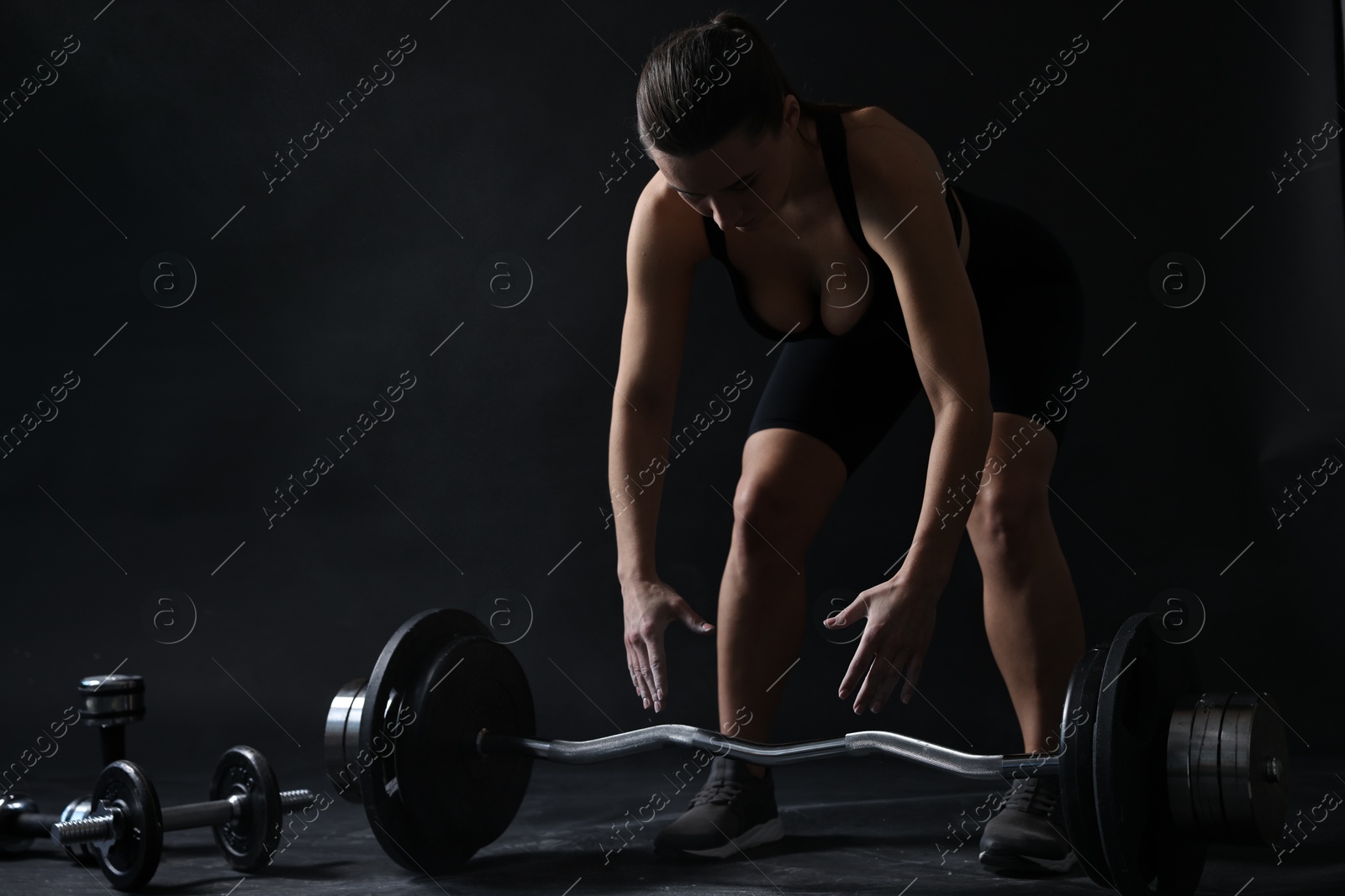 Photo of Woman with talcum powder on hands training with barbell against black background