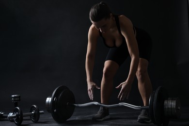 Photo of Woman with talcum powder on hands training with barbell against black background