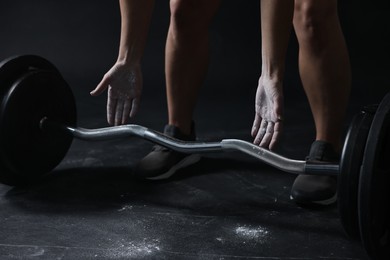 Photo of Woman with talcum powder on hands training with barbell against black background, closeup