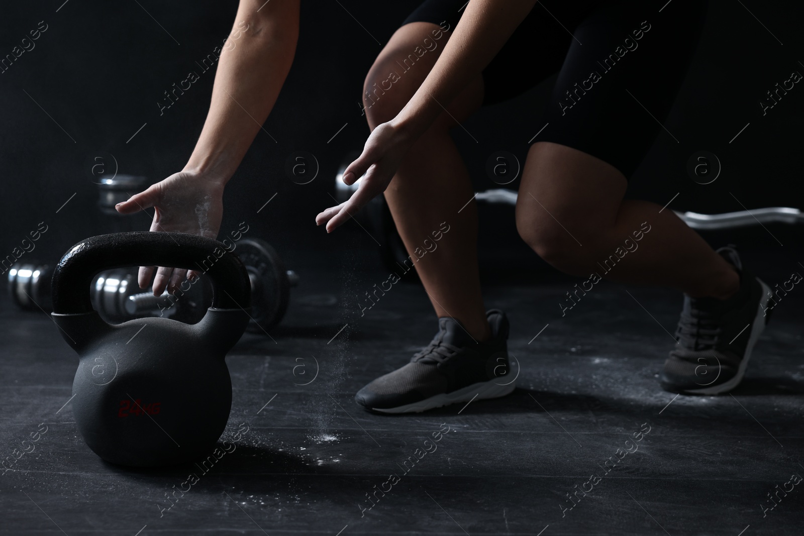 Photo of Woman with talcum powder on hands training with kettlebell against black background, closeup