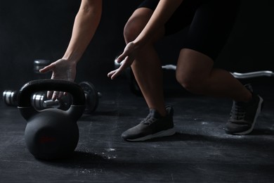 Photo of Woman with talcum powder on hands training with kettlebell against black background, closeup