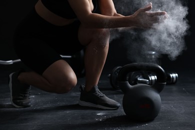 Photo of Woman clapping hands with talcum powder before training with kettlebell on black background, closeup