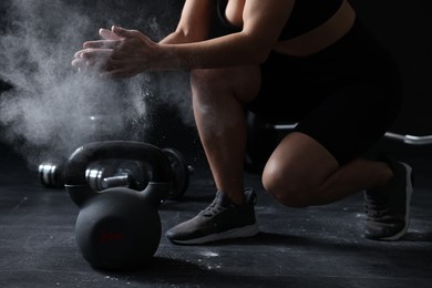 Photo of Woman clapping hands with talcum powder before training with kettlebell on black background, closeup