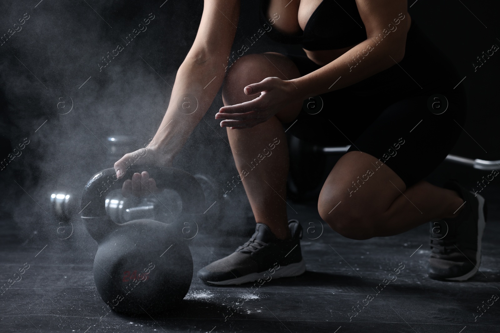 Photo of Woman with talcum powder on hands training with kettlebell against black background, closeup