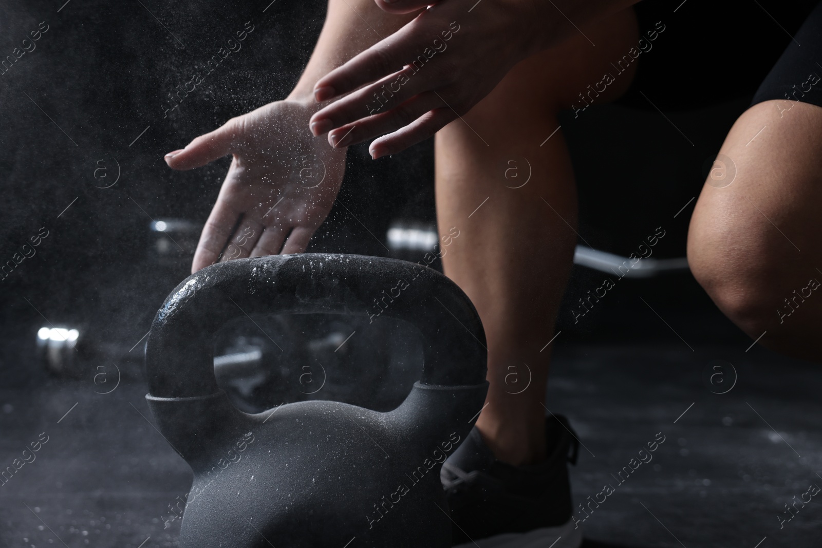 Photo of Woman with talcum powder on hands training with kettlebell against black background, closeup