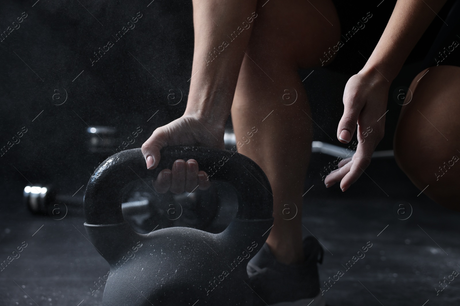 Photo of Woman with talcum powder on hands training with kettlebell against black background, closeup