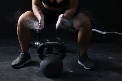 Photo of Woman clapping hands with talcum powder before training with kettlebell on black background, closeup